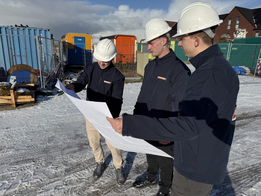 Bouwteam in donkerblauwe jassen bestudeert een uitgeklapte tekening naast opslagcontainers in de sneeuw